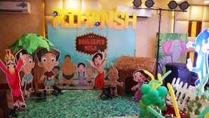 Un área de juegos infantiles con personajes de caricaturas, un letrero que dice "DHOLAKPUR MELA" y un escenario con luces.