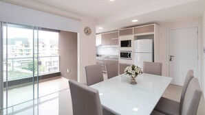 Une cuisine moderne dotée d’appareils électroménagers intégrés, un coin repas avec une table et des chaises blanches, et une grande fenêtre offrant une vue sur la ville.