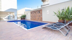 Une piscine entourée d’une terrasse en bois, de chaises longues et de plantes en pot.