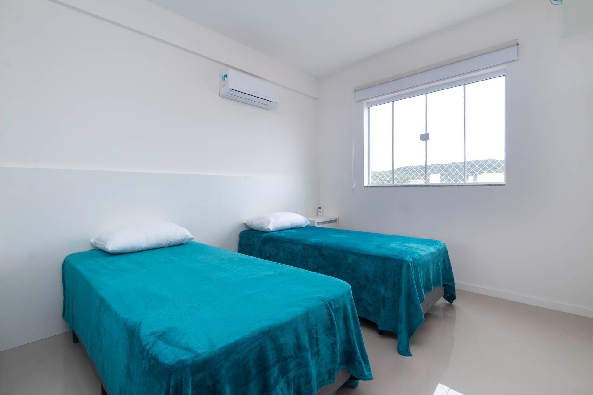 Una habitación con dos camas, una ventana y un equipo de aire acondicionado.