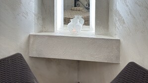 Una ventana estrecha con marco blanco, un jarrón pequeño y una cama que se ve en el reflejo.