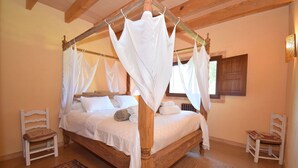 Ein Bett mit Baldachin und weißen Leinen, ein hölzernes Kopfende und ein großes Fenster mit Holzläden.