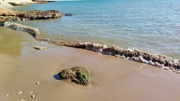 Een strand met helder water, rotsen en een zandstrand.
