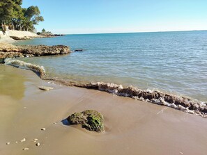 Ein Strand mit klarem Wasser, Felsen und einem Sandufer.
