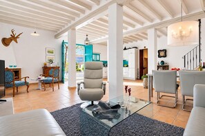 A spacious living area with a glass coffee table, a comfortable sofa, and a high ceiling with exposed beams.
