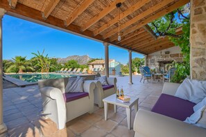 A covered outdoor seating area with a pool, stone walls, and a mountain view.
