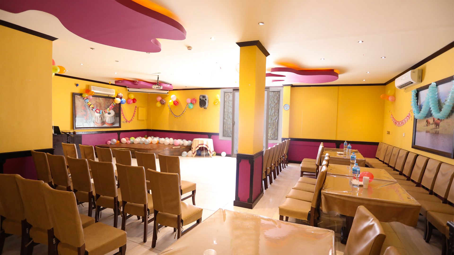 Un salón de conferencias con escenario, sillas, mesas y globos.