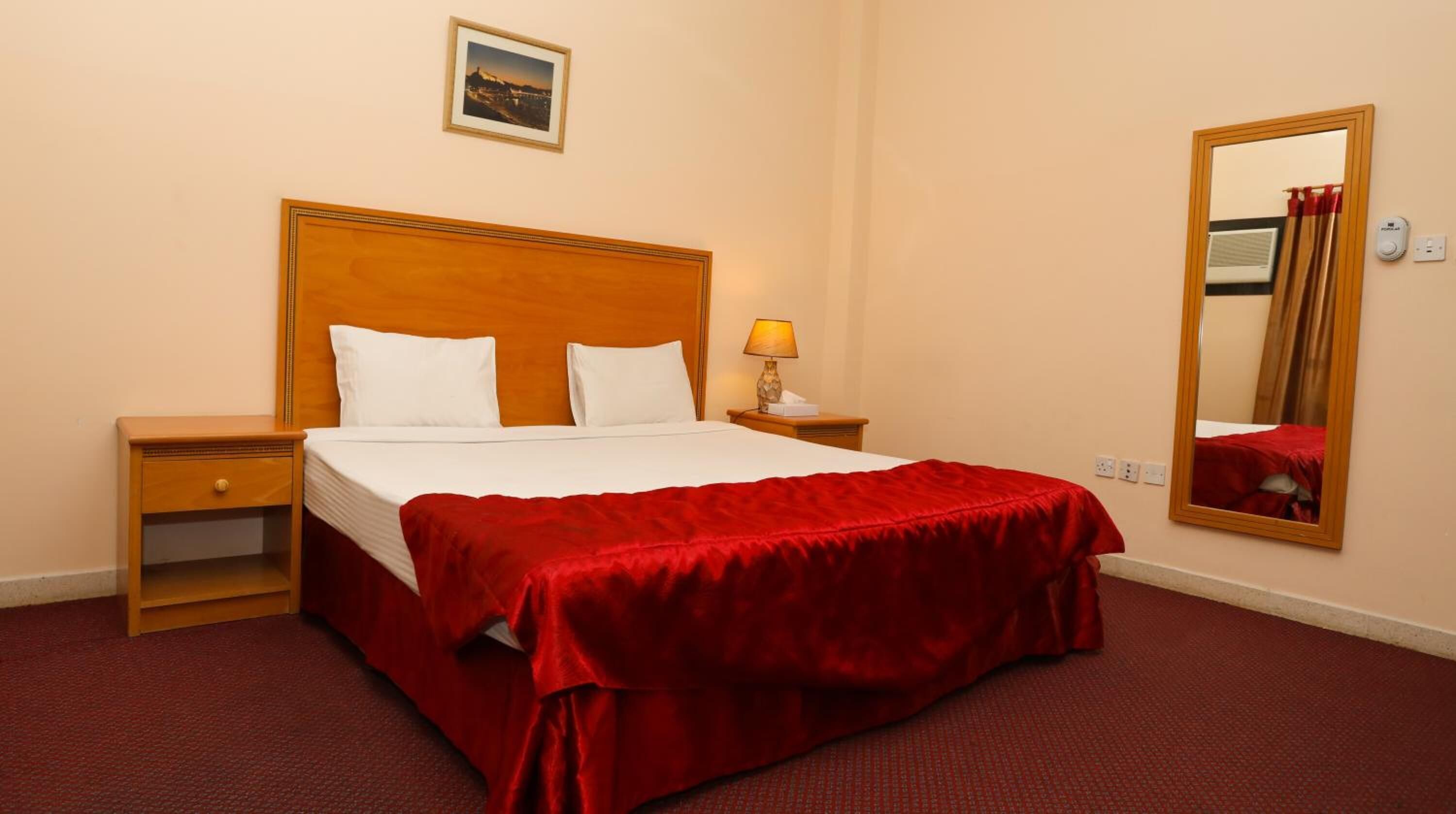 Une chambre d’hôtel avec un grand lit, une tête de lit en bois, une table de chevet avec une lampe, une commode, un miroir et un tableau au mur.
