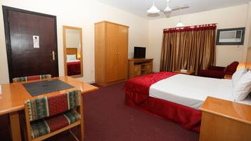 A hotel room with a bed, a desk, a chair, a wardrobe, a television, a mirror, a ceiling fan, and curtains.