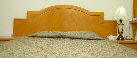 Una cama con un edredón estampado, un cabecero de madera, una lámpara de noche y una mesita de noche con un teléfono y una caja de pañuelos.