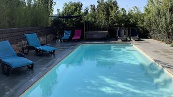A rectangular swimming pool with blue and pink lounge chairs around it.