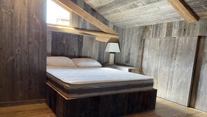 A loft-style bedroom with a wooden slatted ceiling, a bed with a mattress labeled 'Memory', and a nightstand with a lamp. - Savoyard Chalet Authentic (Saint-Martin de Belleville)