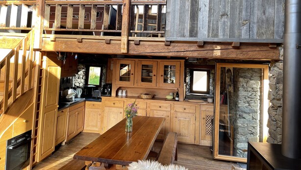 A rustic cabin with a wooden dining area, kitchen with stone walls, and a loft bedroom with a wooden railing. - Savoyard Chalet Authentic (Saint-Martin de Belleville)