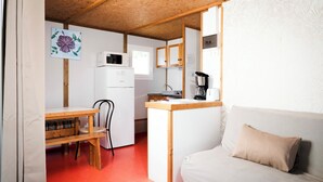 A compact kitchen with a refrigerator, microwave, and coffee maker. There is a wooden table with chairs and a sofa with a cushion.