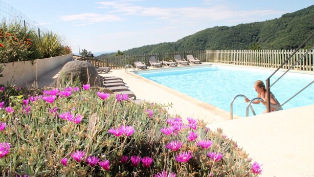 A pool area with lounge chairs, a wooden fence, and a view of a green hillside.