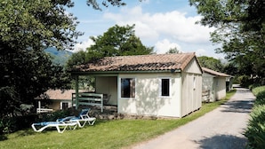 A small, single-story building with a tiled roof, a covered patio with a table and chairs, and a gravel path leading to it.