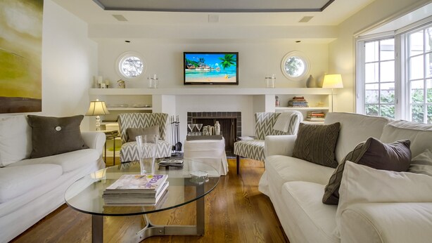 A modern living room with a glass coffee table, white sofas, a fireplace, and a television on the wall. - A Touch of Cape Cod in West Hollywood (West Hollywood)