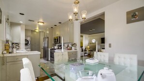 A modern kitchen with white cabinets, stainless steel appliances, and a glass dining table with white chairs. - A Touch of Cape Cod in West Hollywood (West Hollywood)