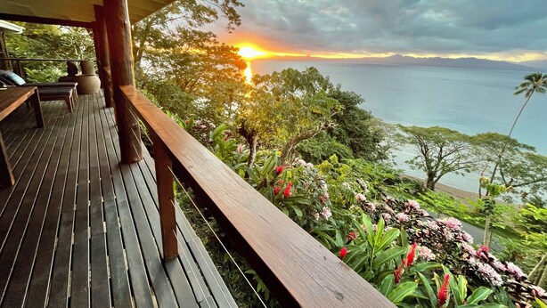 Eine Holzterrasse mit Bänken bietet einen malerischen Blick auf das Meer bei Sonnenuntergang.