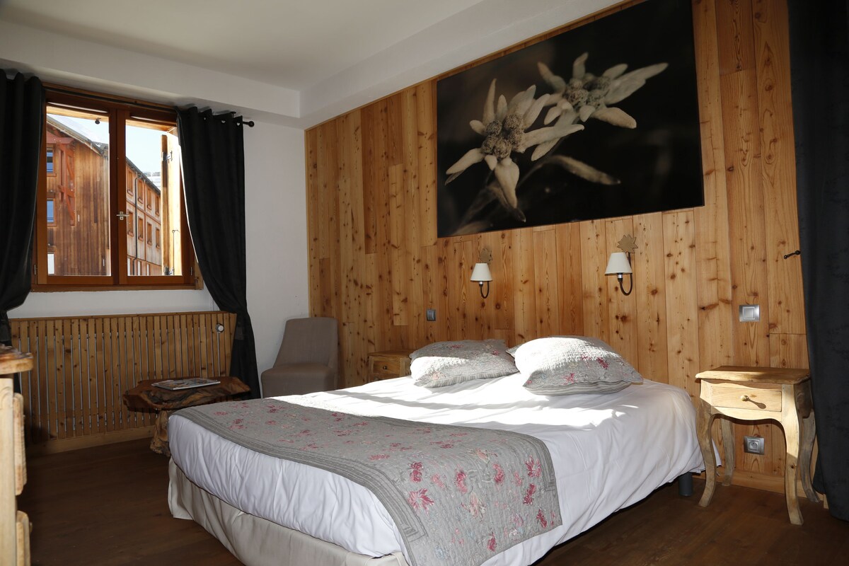 A bedroom with a wooden paneled wall, a bed with white bedding, two bedside lamps, and a window with curtains.