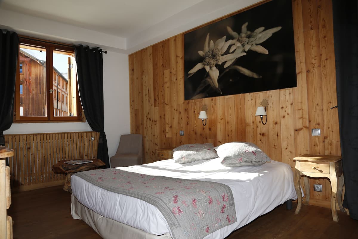 Un dormitorio con una pared de paneles de madera, una cama con ropa blanca, dos lámparas de noche y un ventanal con cortinas.