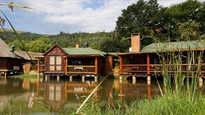 A lakeside lodge with thatched-roof cabins, wooden decks, and a calm water body reflecting the structures. - The Old Orchard (Greater Kokstad)