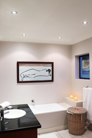 A bathroom with a bathtub, a sink, a framed artwork, and a window with a view.