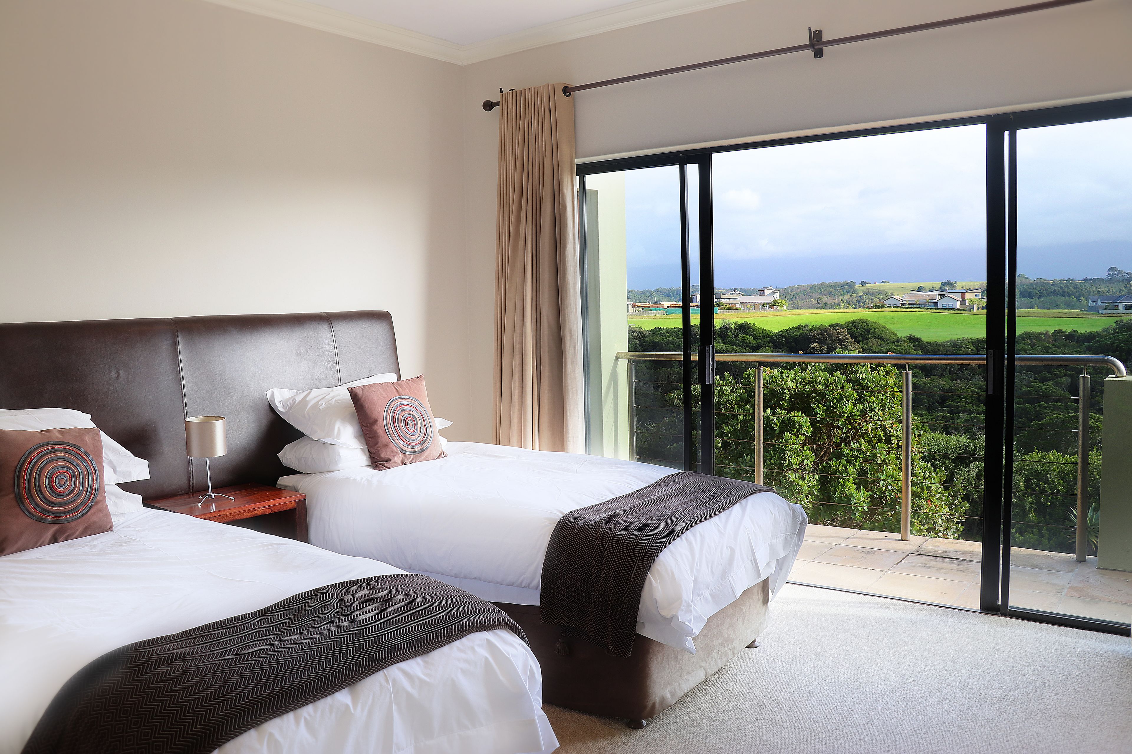 A hotel room with two beds, a large window, and a view of a green landscape.