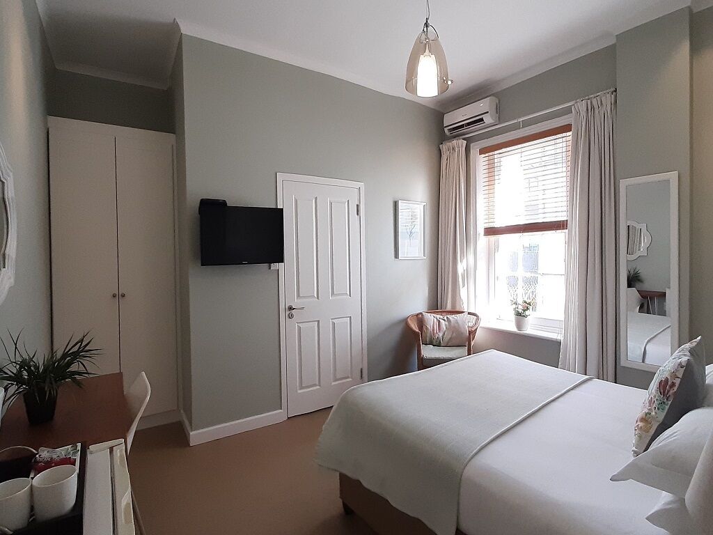 Ein Schlafzimmer mit einem Bett, einem Sessel, einem Fernseher und einem Fenster mit Vorhängen.