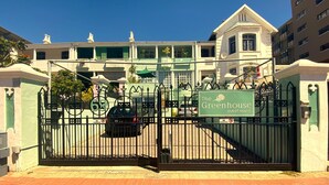 Een hek afsluit een toegang tot een gebouw, met een bord waarop 'The Greenhouse Guest House' staat.
