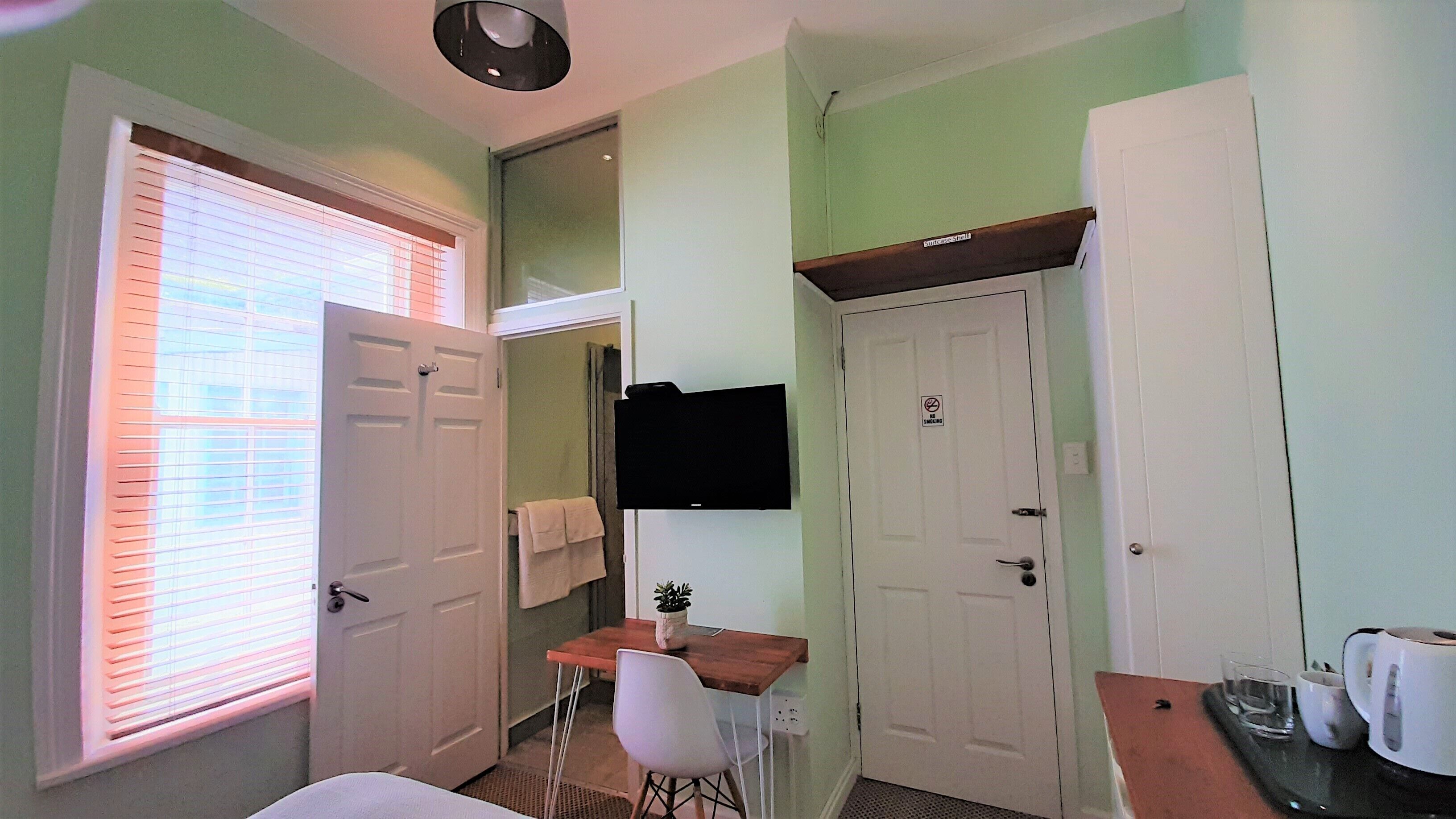 A small, clean room with a bed, a desk, a chair, a TV, and a door with a 'no smoking' sign.