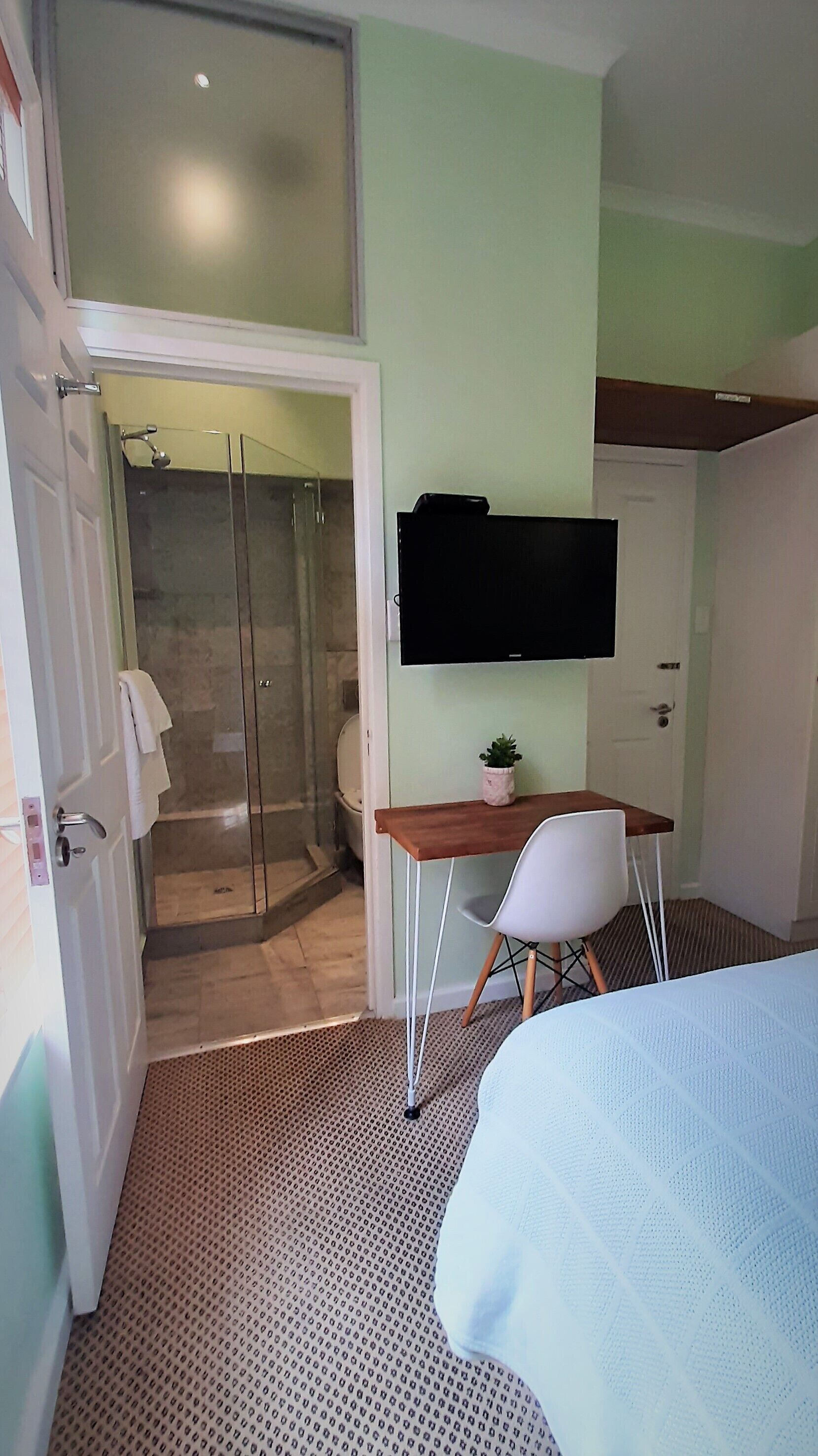 A hotel room with a shower, a desk with a chair, a bed, and a TV mounted on the wall.
