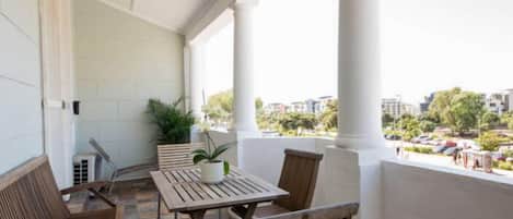 A balcony with a table and chairs, potted plants, and a view of the cityscape.
