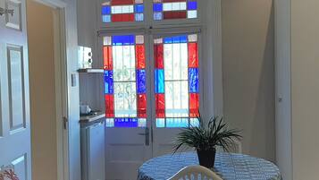 Una habitación con una puerta decorada con vidrieras, una pequeña mesa con una planta y una silla blanca.