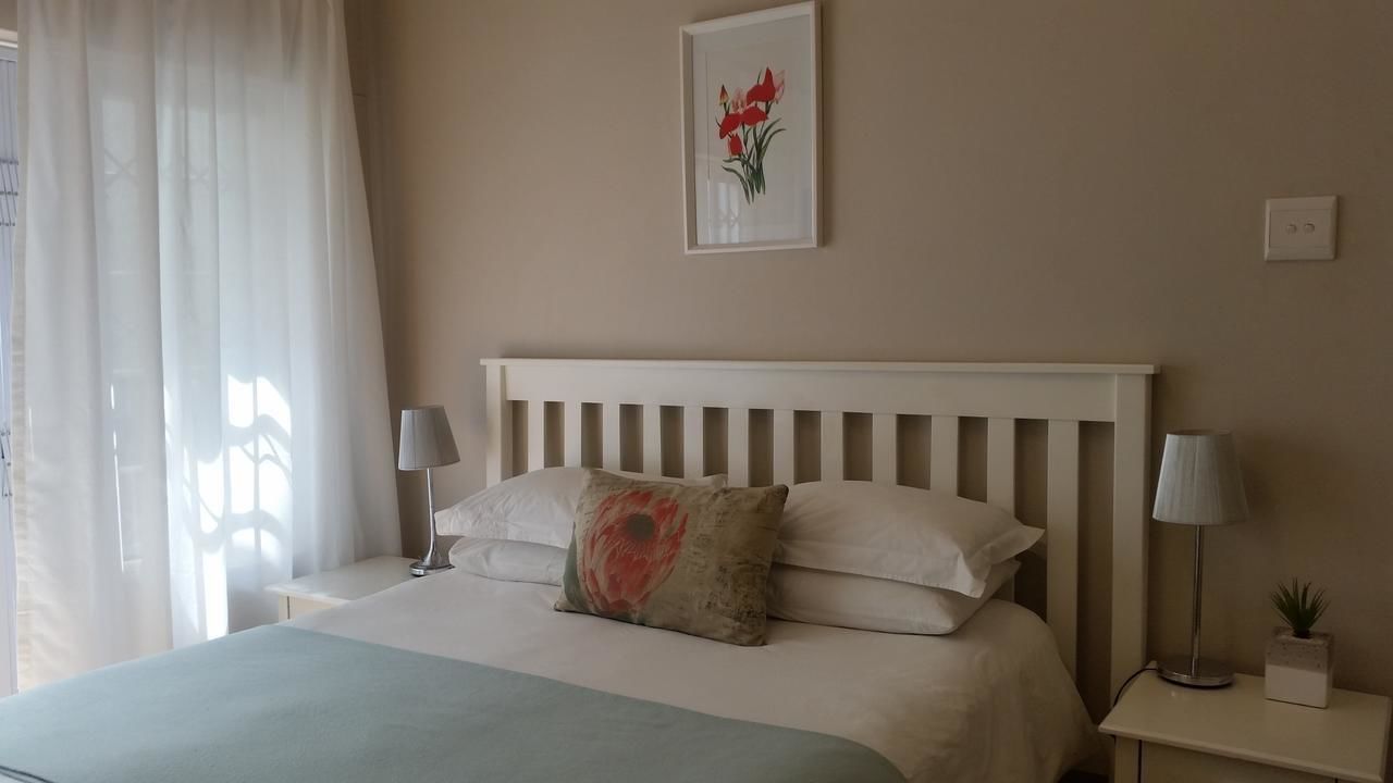 A neatly made bed with a white headboard, two bedside lamps, and a framed picture on the wall.