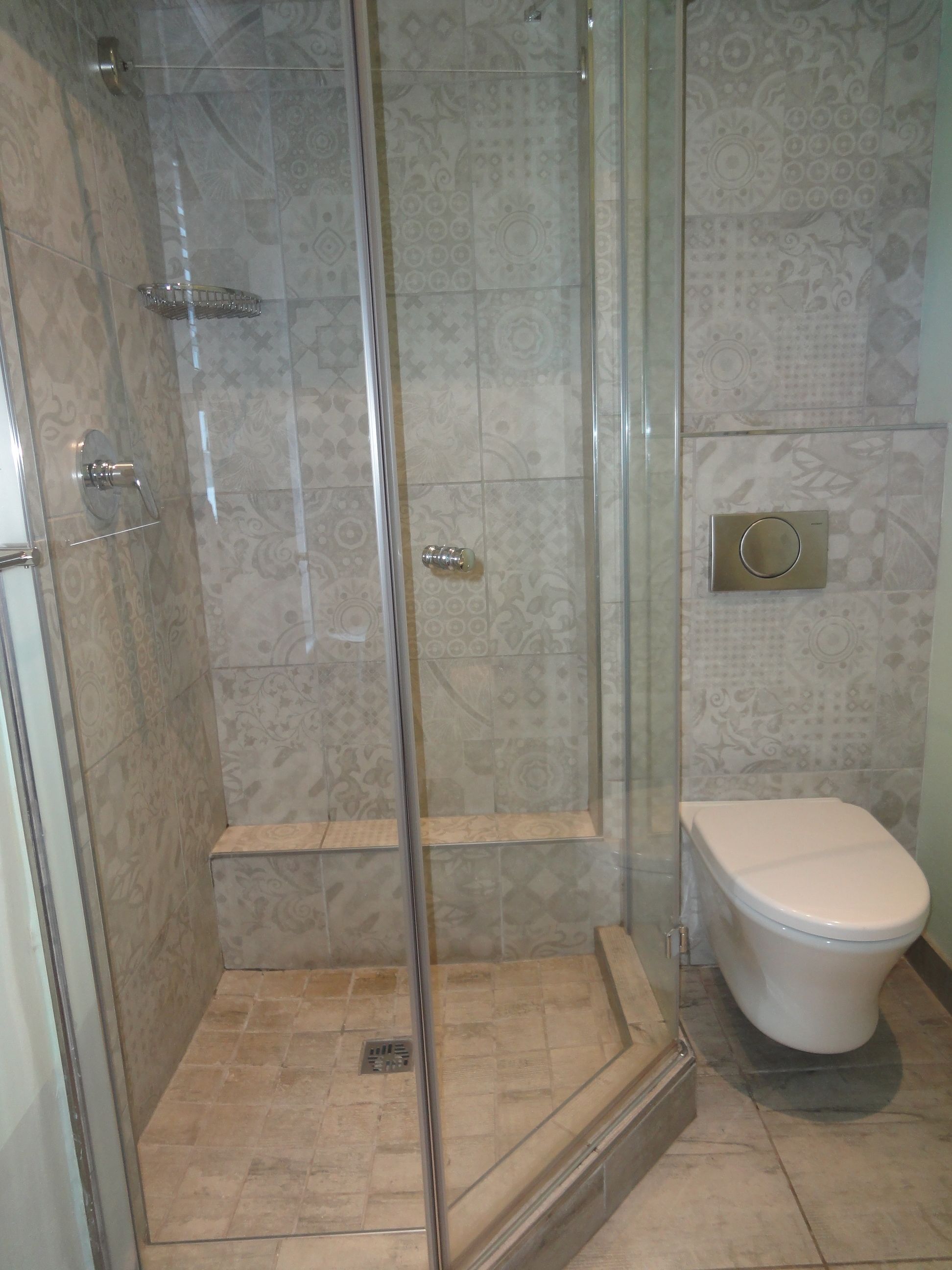 A shower with a glass door, a toilet, and patterned tiles.