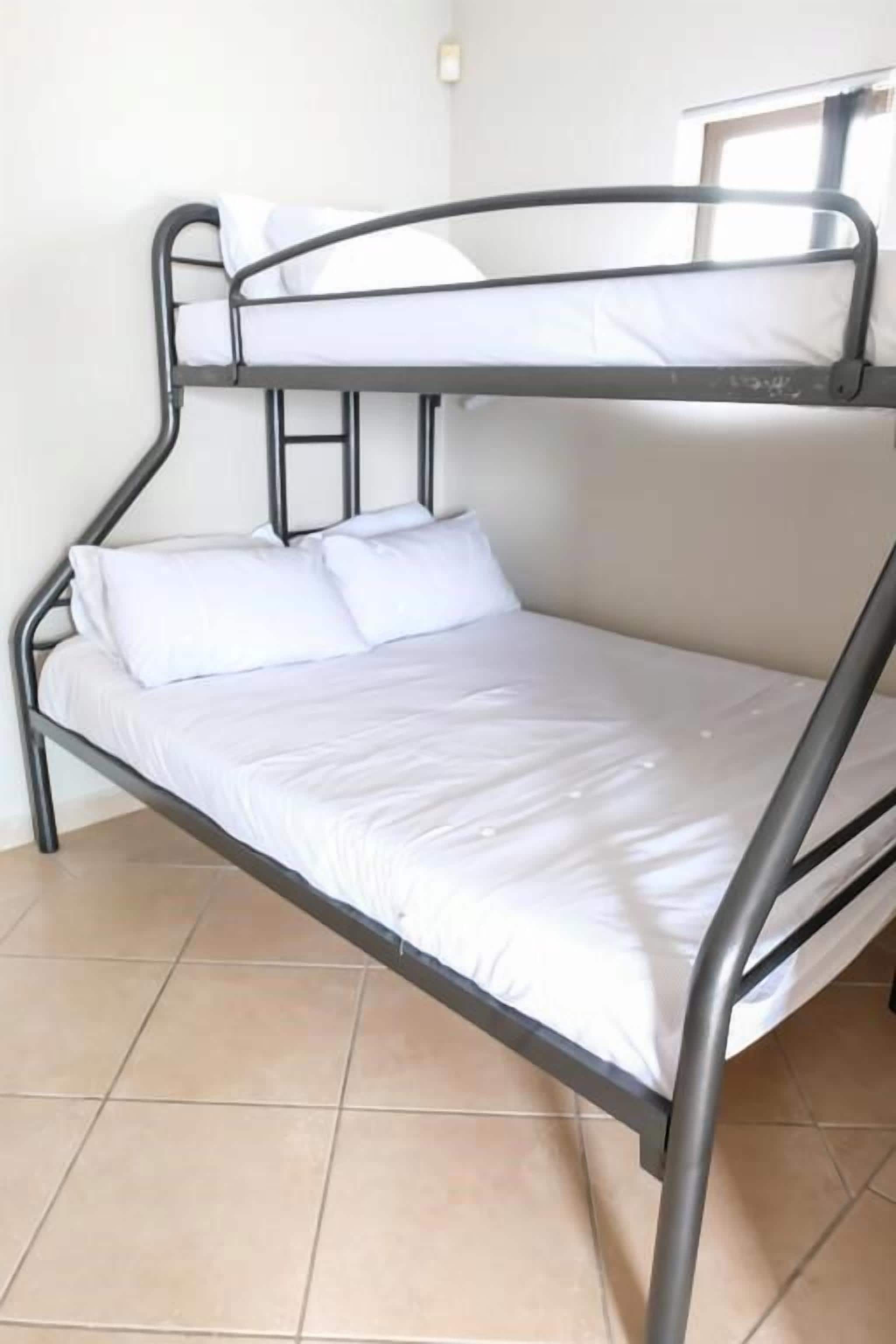 A bunk bed with white bedding in a room with tiled flooring.
