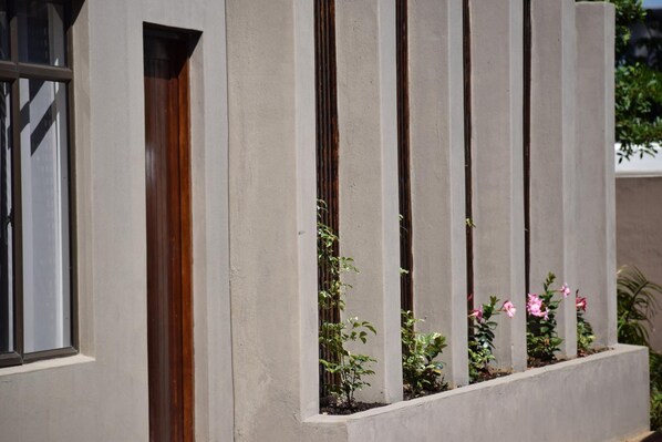 A building facade with vertical concrete columns, a wooden door, and small plants in window boxes. - Beach Retreat Guest House (aManzimtoti)