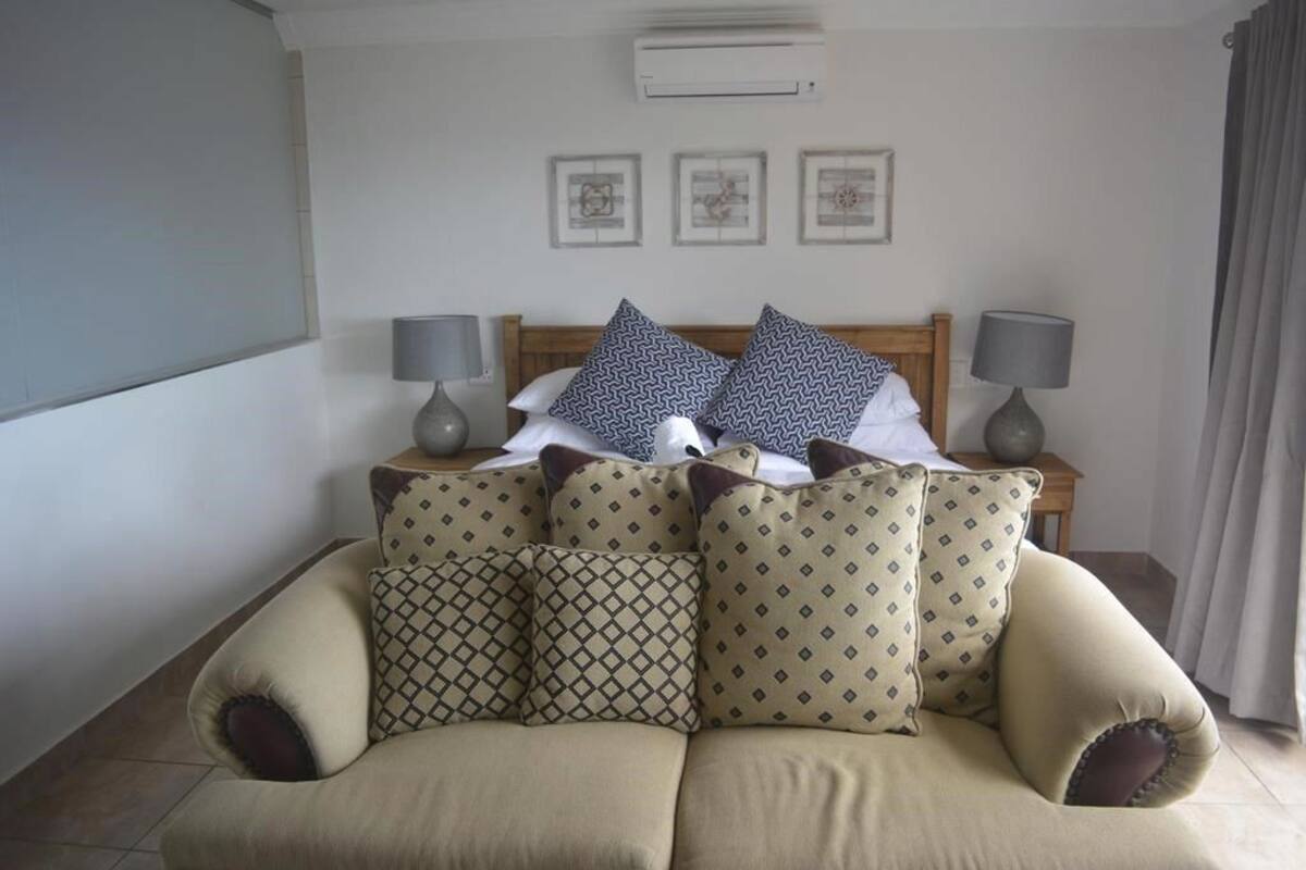 A bedroom with a bed, two bedside tables with lamps, a sofa, and a wall-mounted air conditioner.