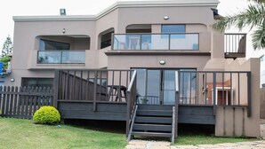 Een modern huis met twee verdiepingen, een balkon en een trap naar de ingang, met een omheinde tuin.