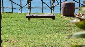 A swing set with ropes and a wooden seat, positioned on a grassy area with a view of the ocean.
