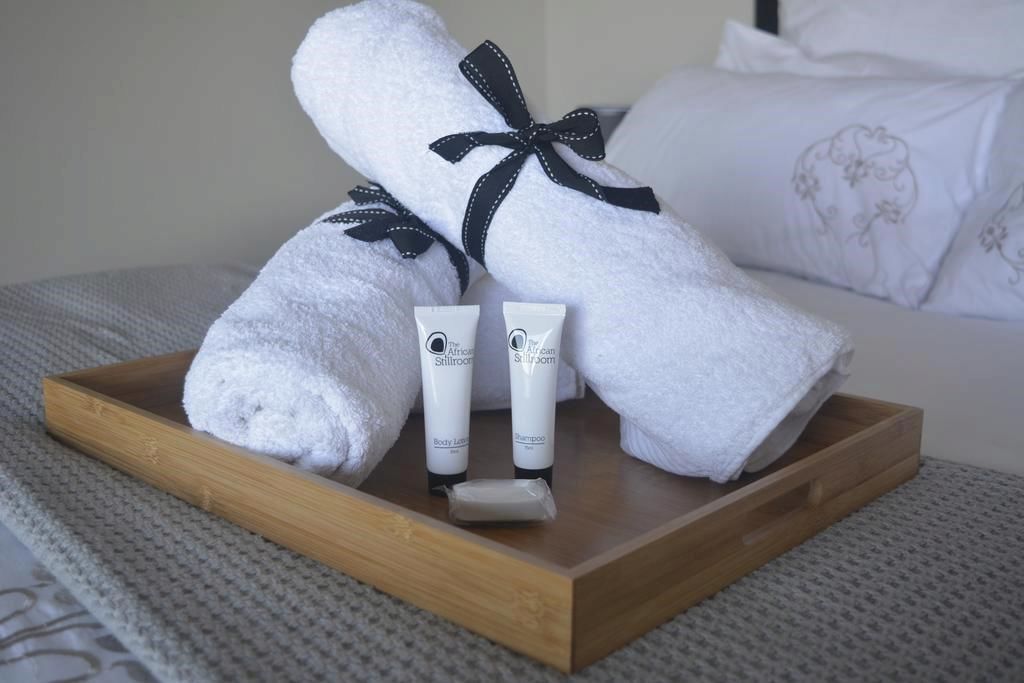 Un plateau en bois avec deux serviettes blanches attachées par des rubans noirs, une lotion pour le corps et un flacon de shampoing.