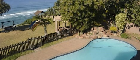 A swimming pool with a view of the ocean, surrounded by a wooden fence and tropical vegetation.