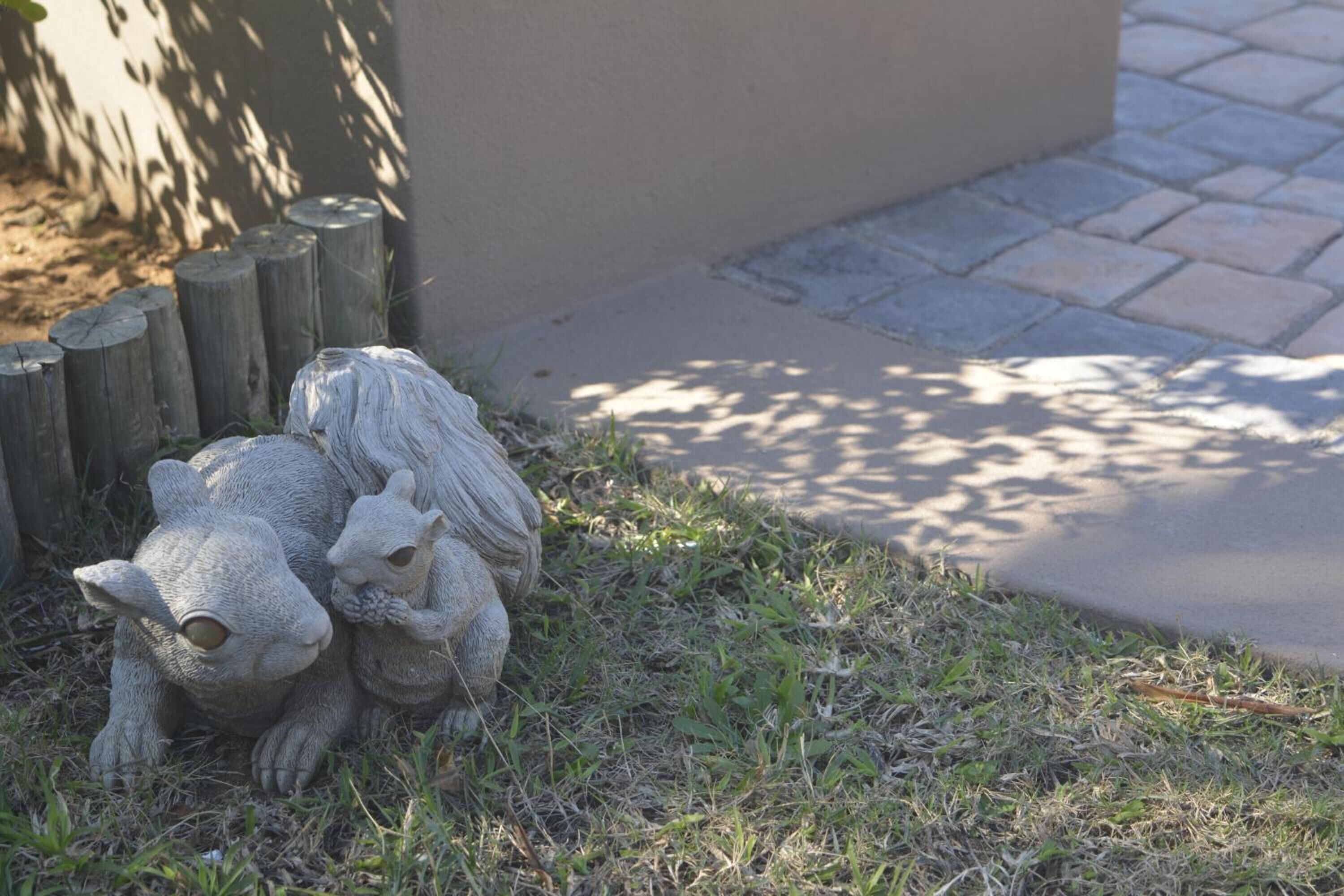 A garden statue of a bear and a cub on a grassy area next to a paved path.