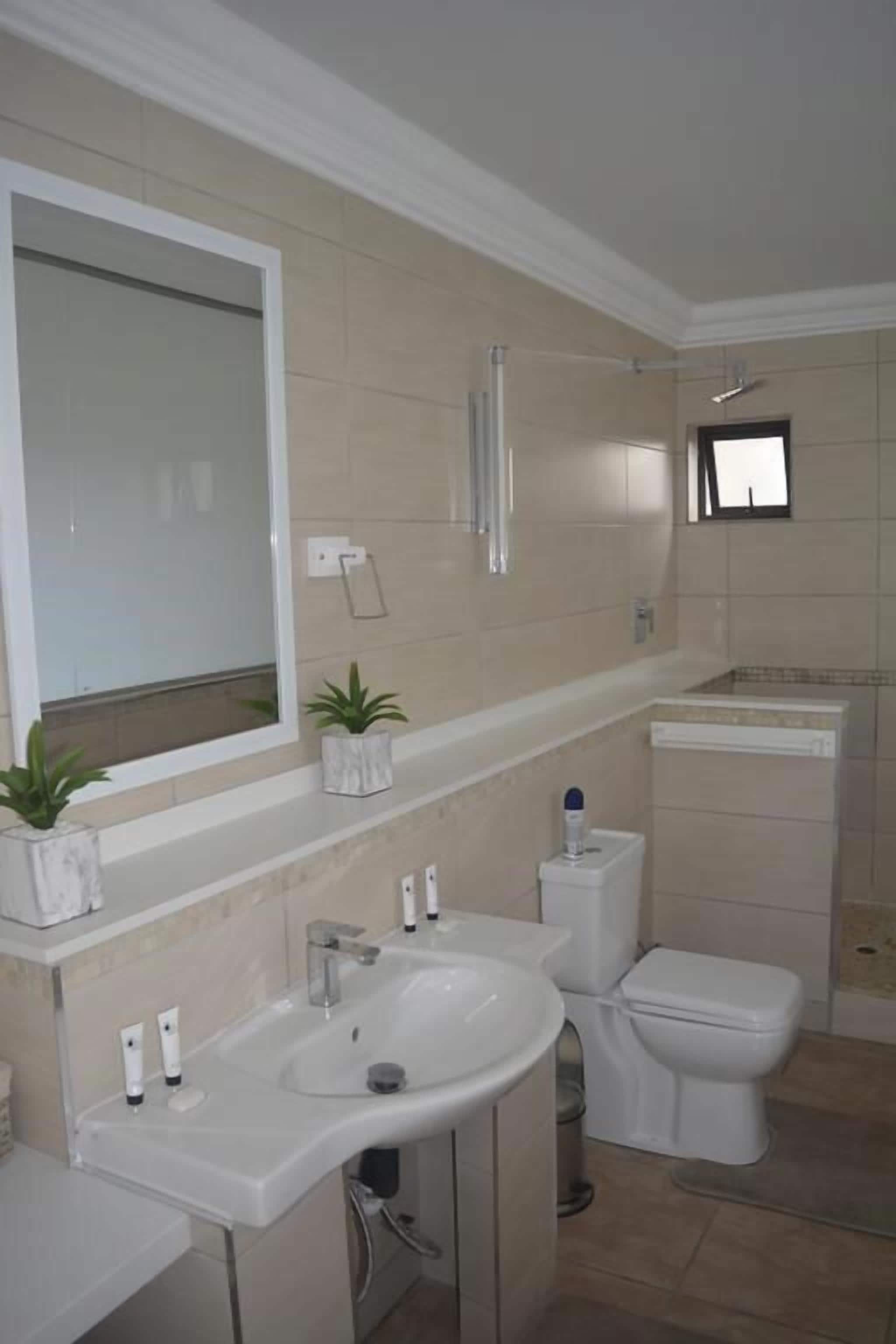 A bathroom with a large mirror, a sink, a toilet, and a shower area.