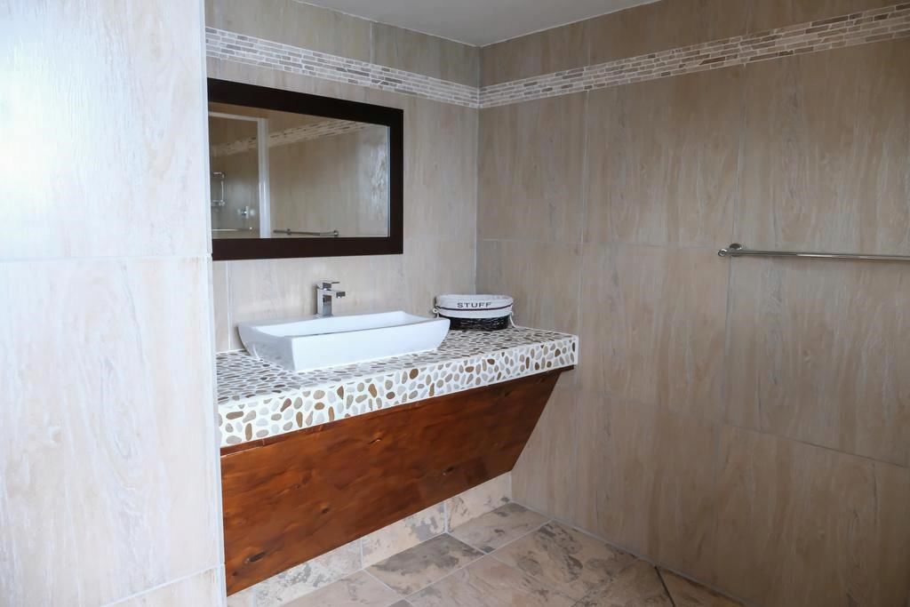 Un baño con lavamanos blanco, tocador de madera, espejo y toallero.