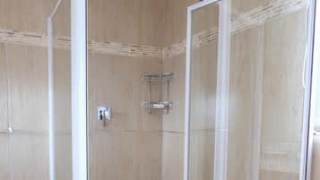 Une douche à l’italienne avec une porte en verre, des murs carrelés et un pommeau de douche.
