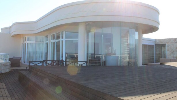 A modern building with a curved facade, large glass windows, and a wooden deck. - Unit 1101 Oyster Rock (Umhlanga)