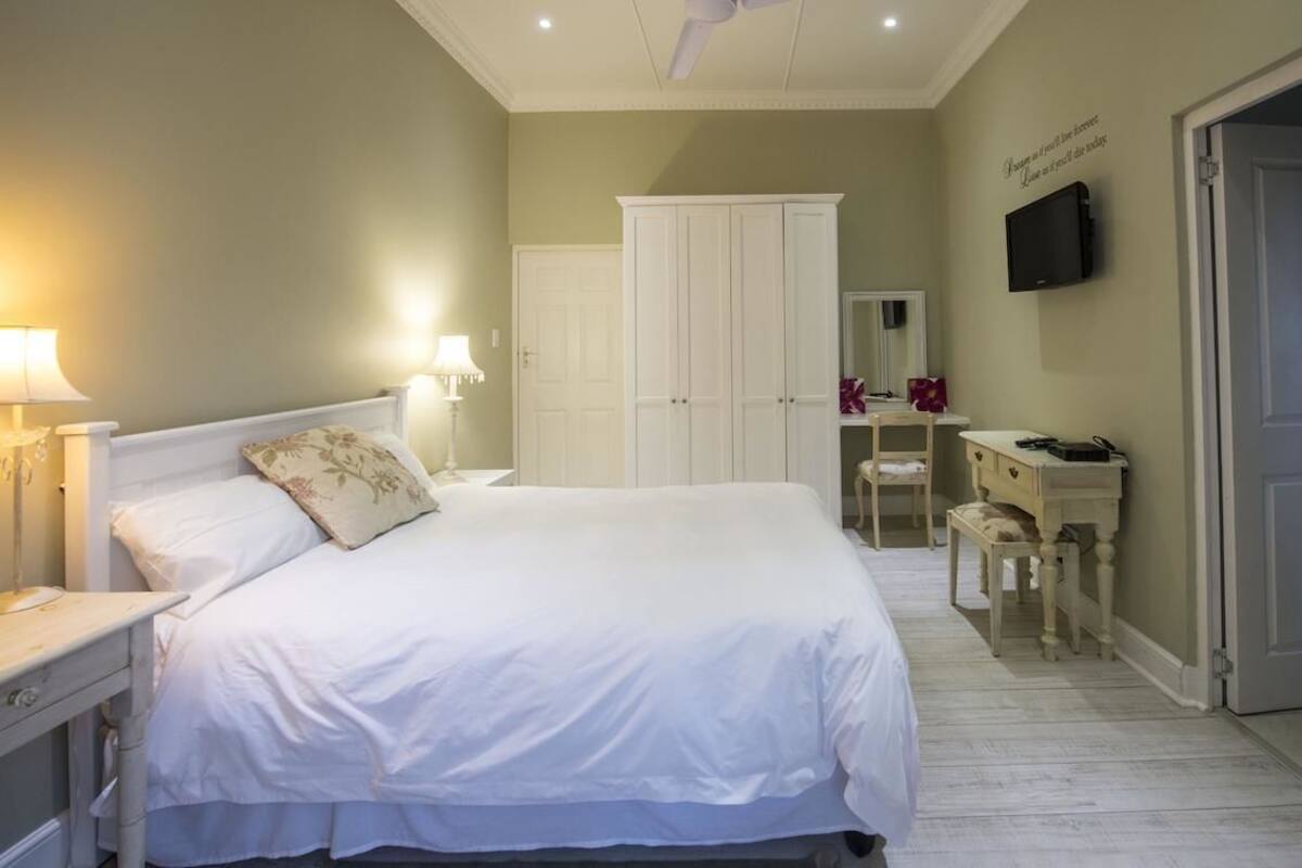 A bedroom with a large bed, bedside lamps, a wardrobe, a vanity with a mirror, and a television on the wall.