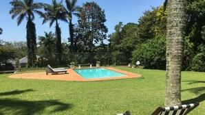 A swimming pool surrounded by grass, with two striped lounge chairs and a bench. - Lemon Tree B&B (Kloof)